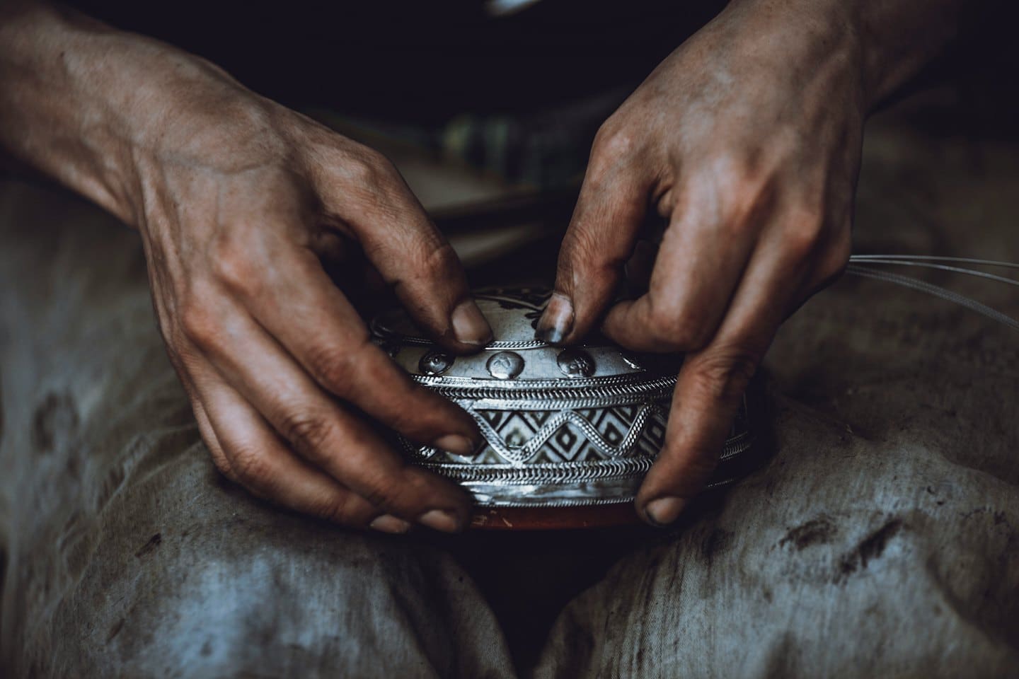Hands carefully attaching fine wires to a decorative metal object.