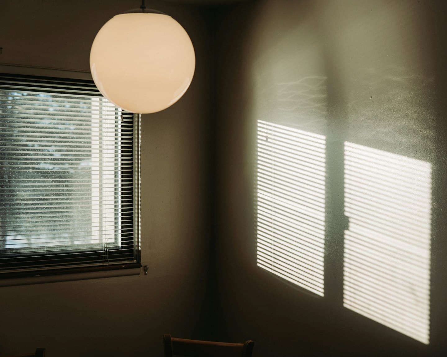 A round ceiling light hangs beside a window with blinds.